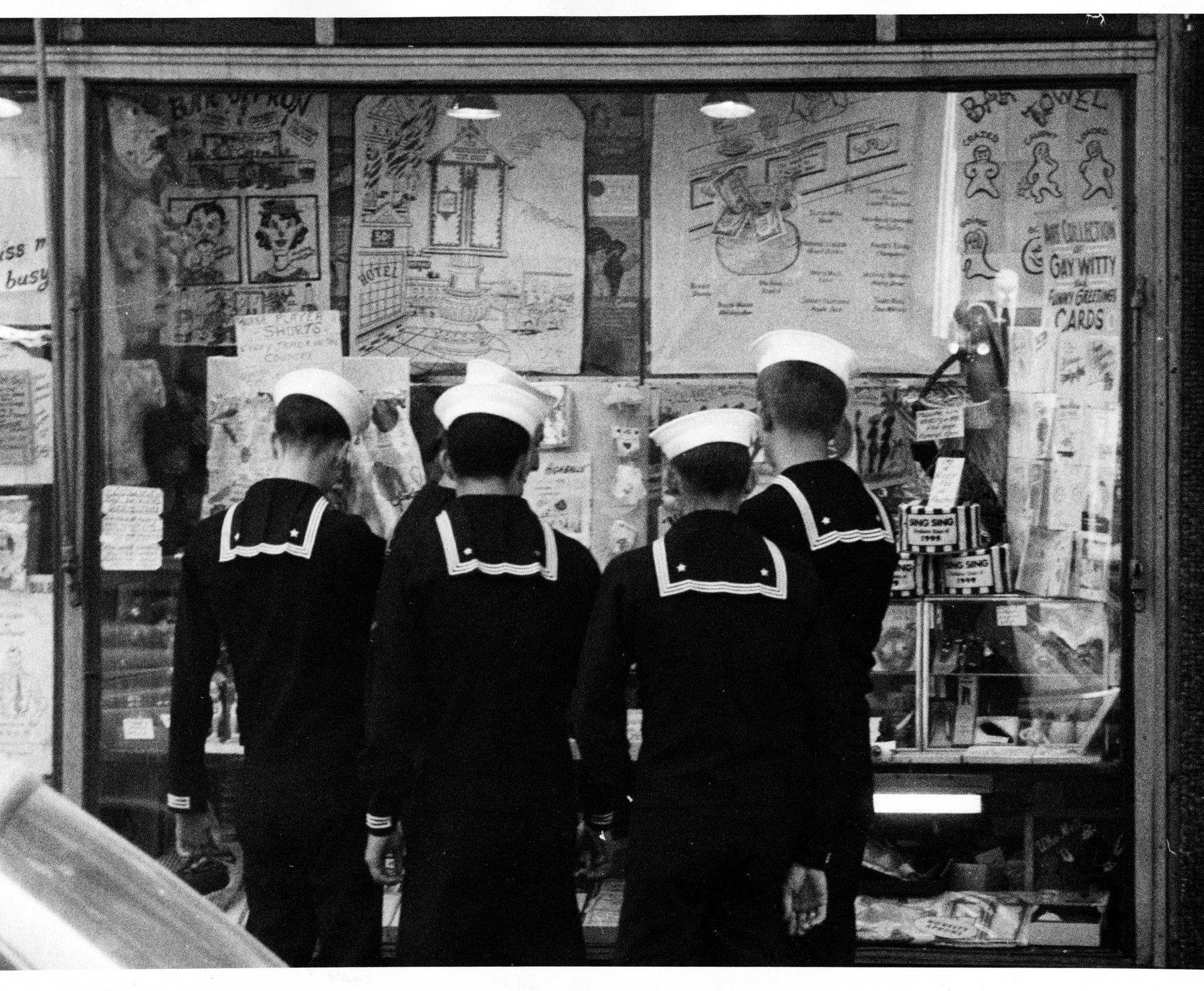 Four sailors, seen from behind, looking into a shop window.