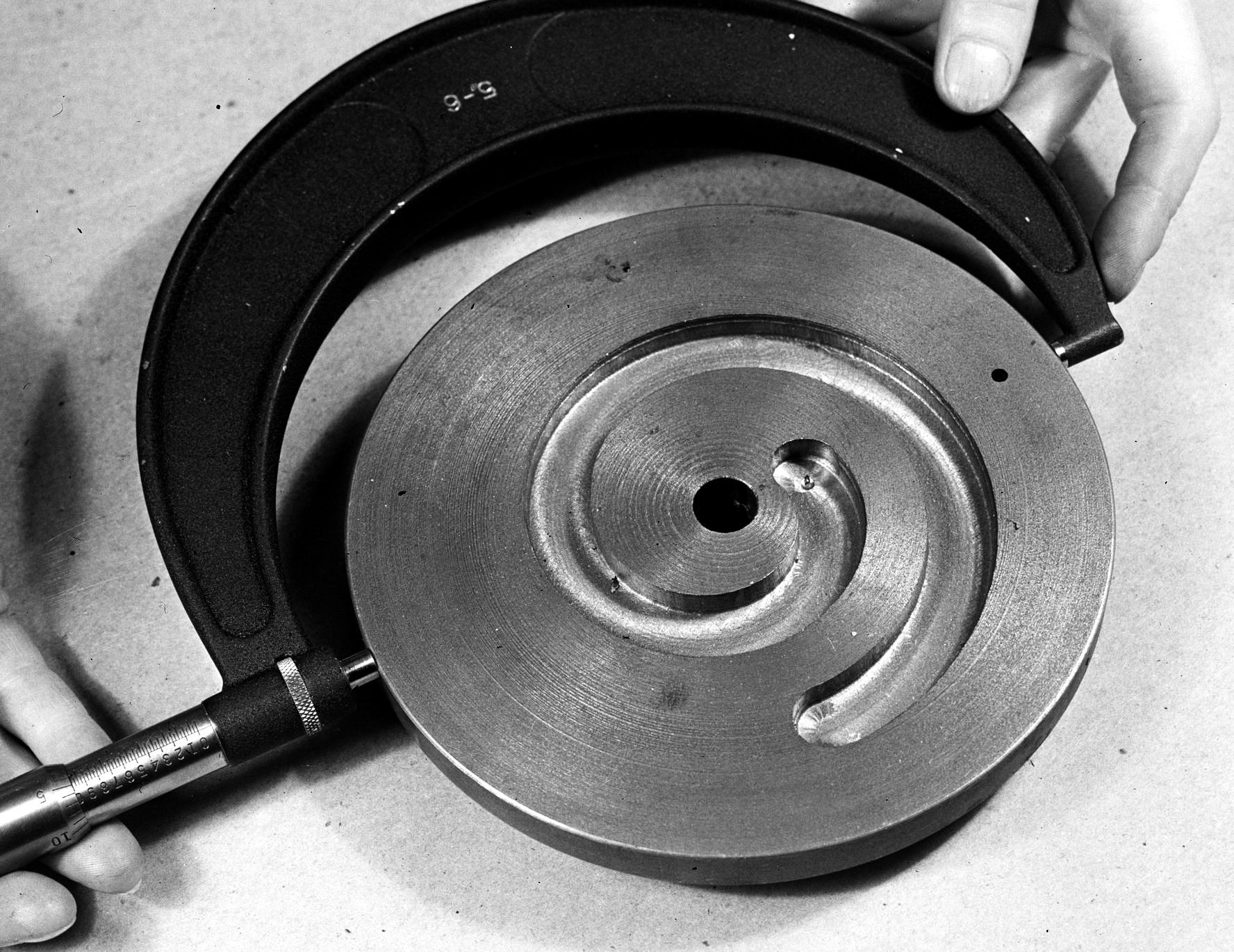 Two hands closing a micrometer on a machined disc.