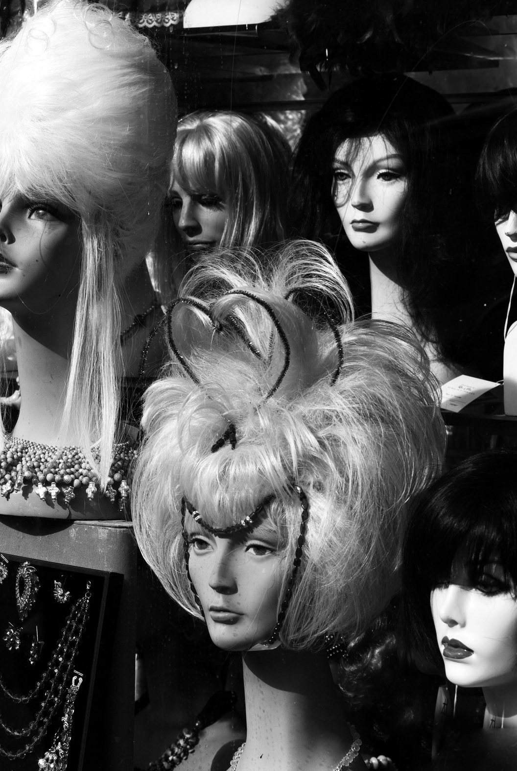 Two mannequin heads in the wig window, styled against each other.